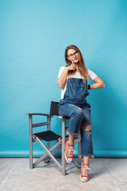 Studio kopya alanı ile uzun boylu bir sandalyede oturan mavi bir arka plan üzerinde çekini parmağınızla dokunmak ise bir düşünceli yüz ifadesi yapma coquette hamile kadın.
