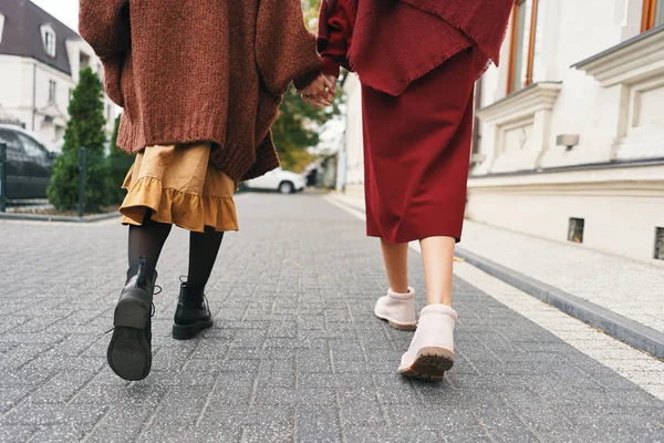 Fall winter fashion outfit details. Back view cropped image of two stylish girls walking on city street. Set of wool clothes, shoes and accessories.