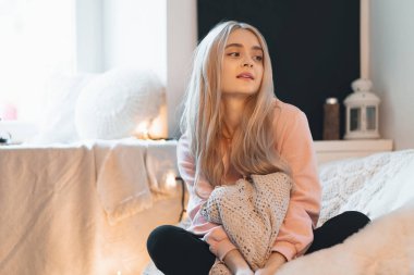 Sevimli Genç kız bağdaş rahat bir yuvarlak koltukta evde oturuyor. Bir soluk pembe parka giyiyor. Mum içinde belgili tanımlık geçmiş penceresinde.