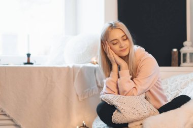 Sevimli Genç kız bağdaş rahat bir yuvarlak koltukta evde oturuyor. Bir soluk pembe parka giyiyor. Mum içinde belgili tanımlık geçmiş penceresinde.