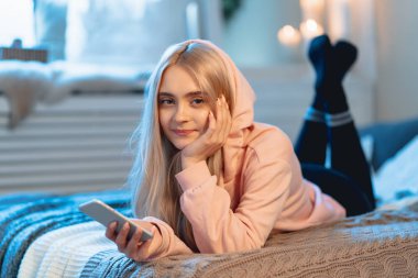 Sarışın kız pembe parka ve arkadaşları ile sohbet ederken evde, yatakta yatıyordu bir akıllı telefon kullanarak siyah tozluk gülümseyen