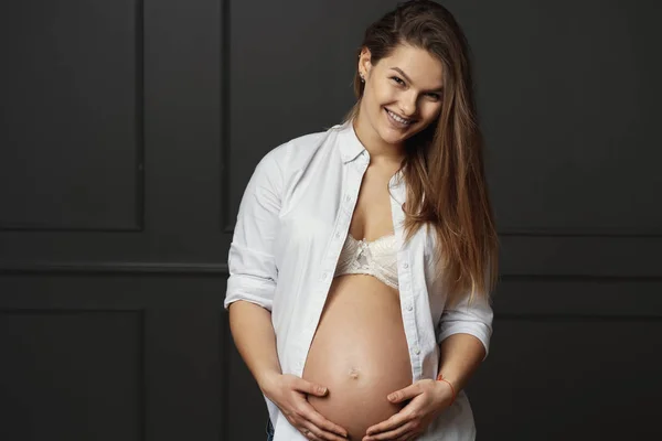 Splendida giovane donna incinta che tocca delicatamente con le mani la pancia, inviando amore al suo nascituro — Foto Stock