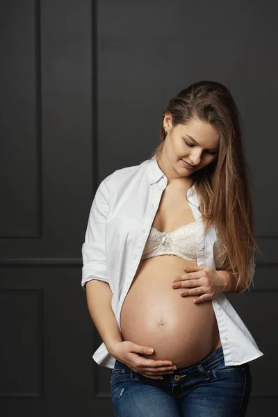 Wunderschöne junge schwangere Frau berührt sanft mit den Händen ihren Bauch und sendet Liebe zu ihrem ungeborenen Baby — Stockfoto