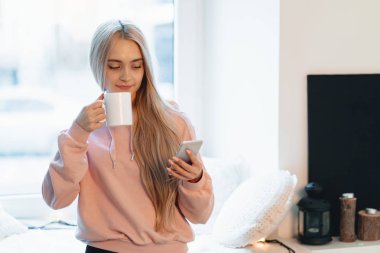 Kapalı pencerelerde bir akıllı telefon kullanırken kahve keyfi Pretty genç kadın