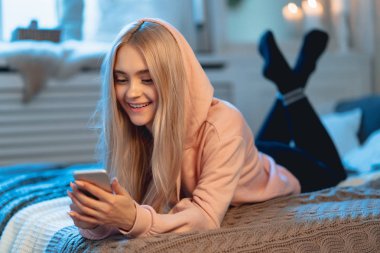 Arkadaşlarıyla sohbet ederken, evde yatakta yatan bir akıllı telefon kullanarak pembe Pretty sarışın kız