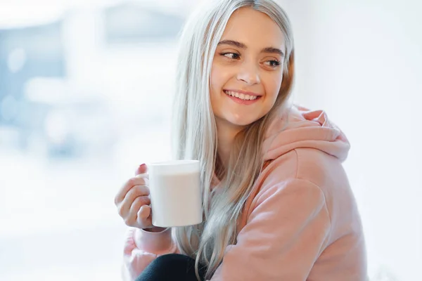 Bir elf hem, genç kız kapalı pencerenin yanında otururken kahve veya süt bir fincan zevk — Stok fotoğraf