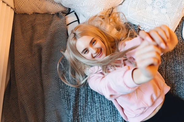 Glimlachend meisje, met lang blond haar, genietend van geluk terwijl liggend op bed thuis — Stockfoto