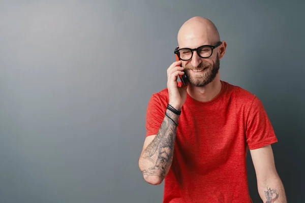 Веселый лысый мужчина в красной футболке разговаривает по телефону и смеется с закрытыми глазами — стоковое фото