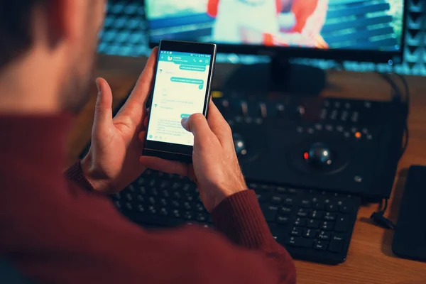 Joven trabajando en el estudio con un smartphone y un ordenador . —  Fotos de Stock