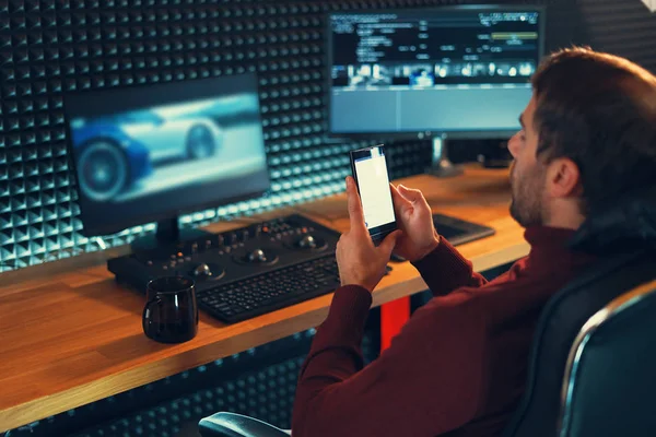 Junger Mann arbeitet im Studio mit Smartphone und Computer. — Stockfoto