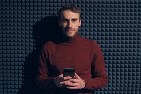 Sonriente hombre confiado sosteniendo teléfono inteligente sobre fondo gris — Foto de Stock