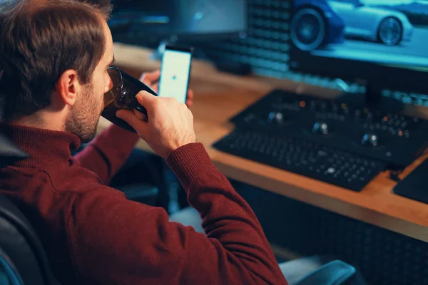 Joven trabajando en el estudio con un smartphone y un ordenador . —  Fotos de Stock