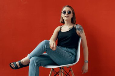 Kırmızı duvarın yanındaki beyaz sandalyede oturan genç kız