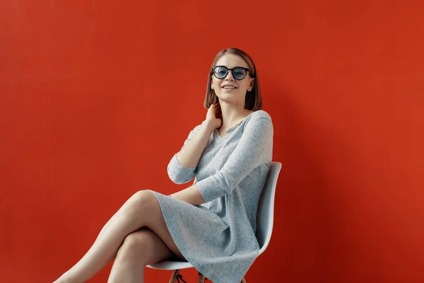 Jeune fille assise sur une chaise blanche près du mur rouge — Photo