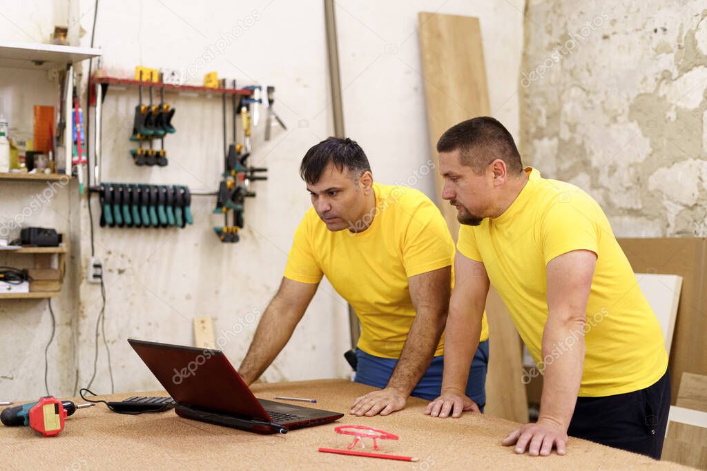 Carpenters using laptop in workshop, searching for a solution