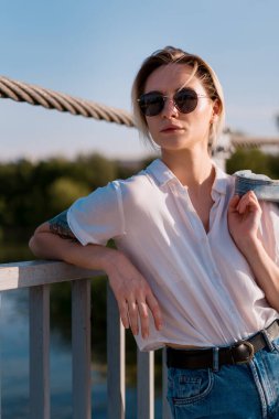 Güneş gözlüklü şık bir kadın köprüde dinleniyor.