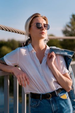 Güneş gözlüklü şık bir kadın köprüde dinleniyor.