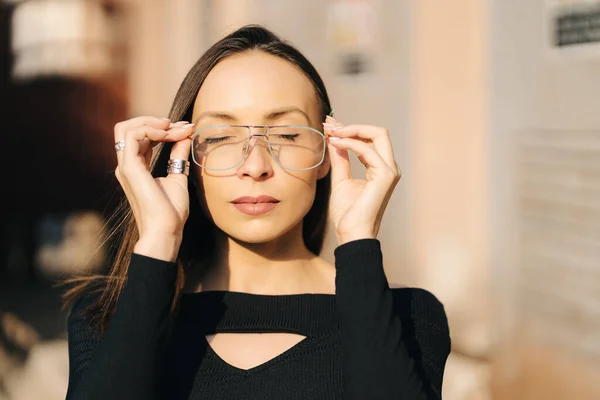 Atractiva joven morena con un top negro y gafas transparentes posando en la calle —  Fotos de Stock