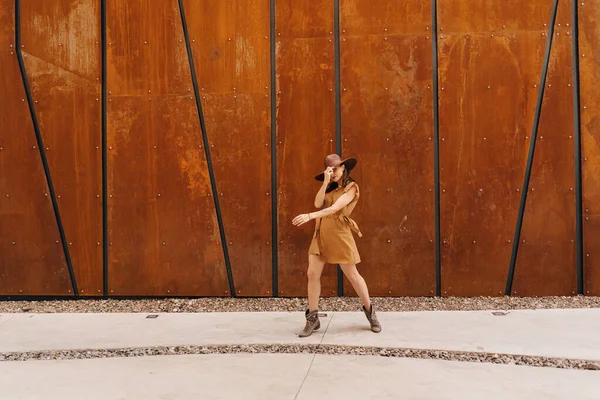 Menina de moda jovem vestida em um vestido de verão com um chapéu largo de vime caminha e posa na cidade velha — Fotografia de Stock