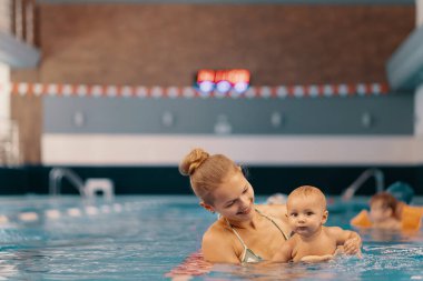 Anne ve küçük oğlu yüzme havuzunda eğleniyor.