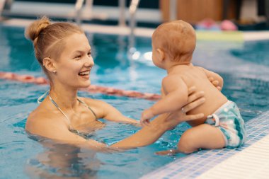 Anne ve küçük oğlu yüzme havuzunda eğleniyor.