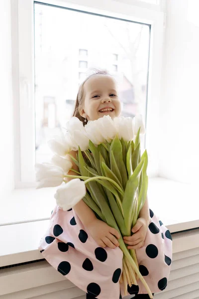 Liten flicka med vita tulpaner nära fönstret — Stockfoto