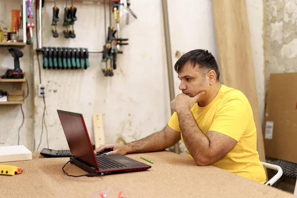 Carpinteiro usando laptop na oficina, procurando uma solução — Fotografia de Stock