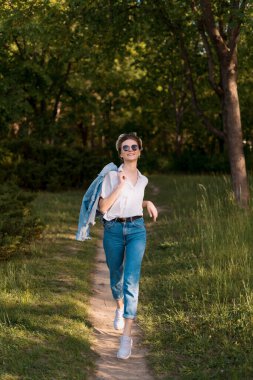 Güneş gözlüklü bir kadın parkta yürüyor.