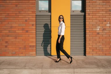 Şehir caddesinde güneş gözlüklü güzel bir kadın yürüyor.