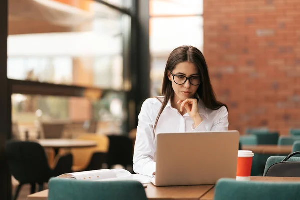 Mooie vrouw in bril praten met behulp van laptop met glimlach terwijl zitten en werken — Stockfoto