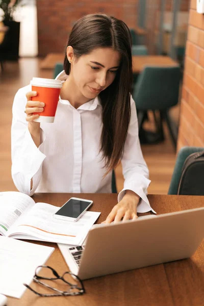 Brunette vrouw drinken koffie te gaan terwijl het werken op laptop — Stockfoto