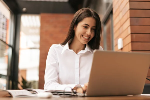 Hermosa mujer en gafas hablando con el ordenador portátil con sonrisa mientras está sentado y trabajando — Foto de Stock