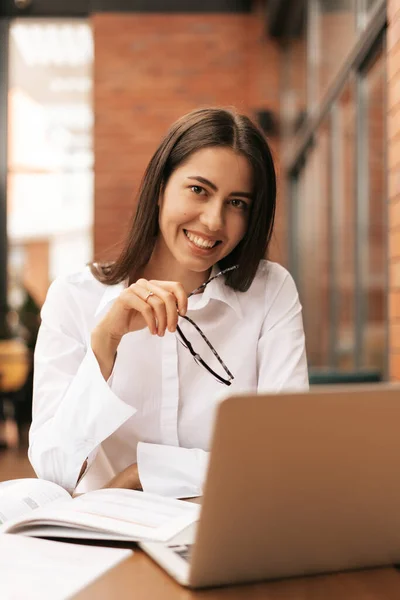 Hermosa mujer en gafas hablando con el ordenador portátil con sonrisa mientras está sentado y trabajando — Foto de Stock