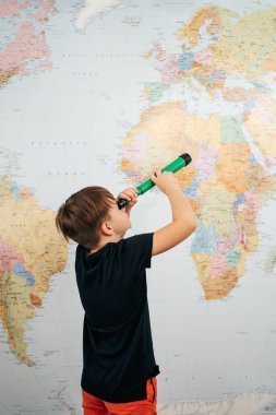 Beyaz bir okul çocuğu teleskopla dünya haritasına bakıyor.