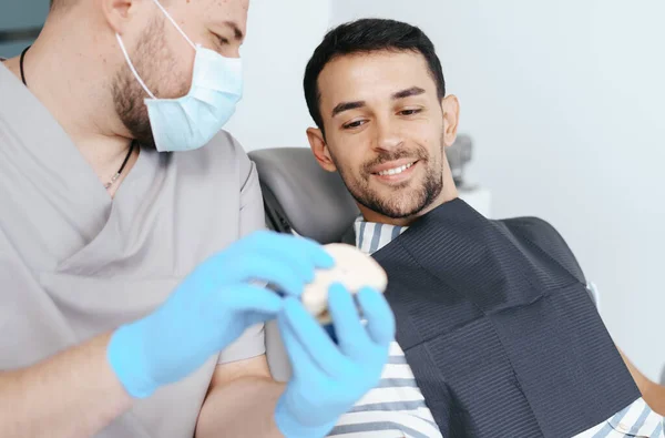 Male dentist showing patient the artificial dentures — Stock Photo, Image