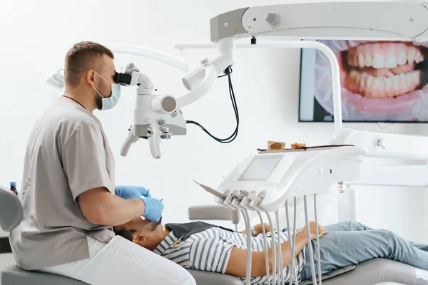 Dentista masculino usando máscara olhando no microscópio — Fotografia de Stock