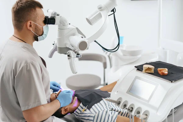 Mężczyzna dentysta w masce patrząc pod mikroskop — Zdjęcie stockowe