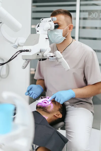 Mannelijke tandarts met masker kijkend in de microscoop — Stockfoto