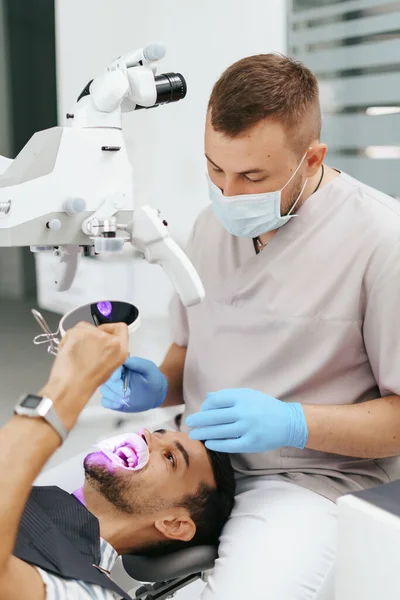 Dokter gigi laki-laki memakai topeng melihat dalam mikroskop — Stok Foto