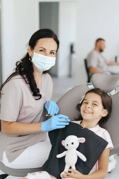 Gyönyörű kislány a fogorvosnál, a kamerába néz és mosolyog. — Stock Fotó