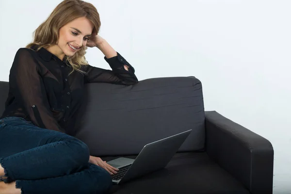 beautiful young girl sitting on the black sofa with a laptop on a white background