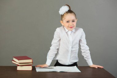 güzel küçük kız kitapları gri bir arka plan ile bir masada oturan ve ödev yapmak başında bir yay ile