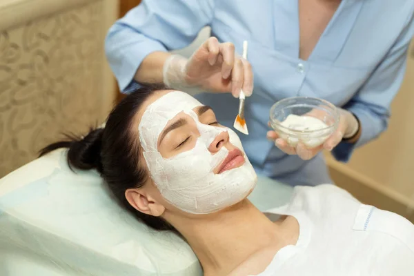 beautiful young girl on a facial treatment in a beauty salon applying a cream