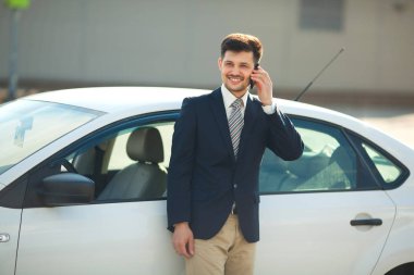 telefonda konuşurken bir araba yakınındaki elbiseli yakışıklı genç adam