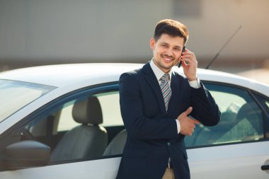 telefonda konuşurken bir araba yakınındaki elbiseli yakışıklı genç adam