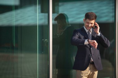 yakışıklı genç adam telefonda konuşurken ve saat bakarak Mimari camlar yakınındaki bir takım ayakta