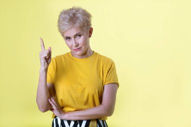 güzel şık yaşlı kadın el hareketi ile sarı zemin üzerine sarı tişört içinde kısa saç modeli ile