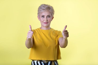 güzel şık yaşlı kadın el hareketi ile sarı zemin üzerine sarı tişört içinde kısa saç modeli ile