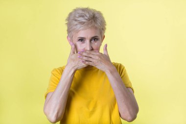 güzel şık yaşlı kadın el hareketi ile sarı zemin üzerine sarı tişört içinde kısa saç modeli ile