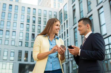 güzel adam ve takım elbiseli, Kız ellerinde telefonları ile yaz aylarında bir binanın zemin üzerine iş tartışıyor